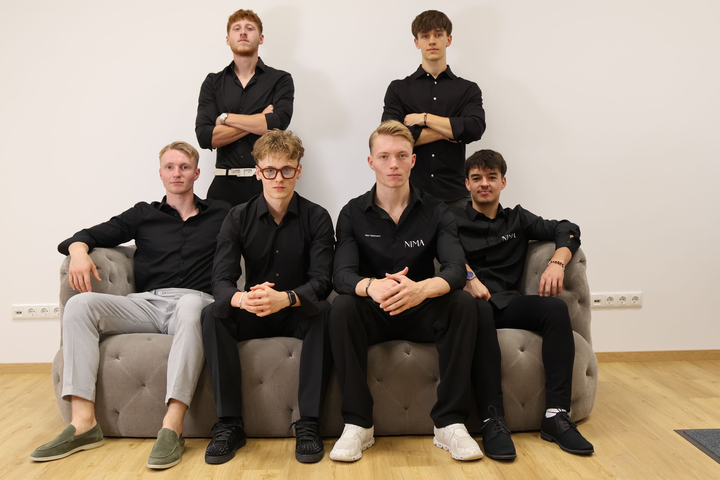 Das Team von NIMA Marketing in Edling – sechs Mitarbeiter in schwarzen NIMA-Hemden auf einem Sofa